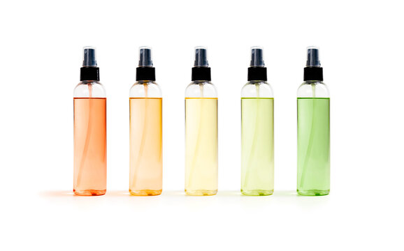 Spray bottles with colorful oil or fragrance, front view. Group of plain product sprayers with red, orange, yellow and green translucent liquid. Cooking spray or beauty products. Isolated on white.