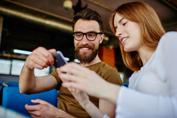 Happy male and female best friend communicate during positive meeting for discussing content plan for website, cheerful hipster guys using cellphone application for browsing media page in networks