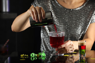 Woman pouring cocktail into glass indoors, closeup