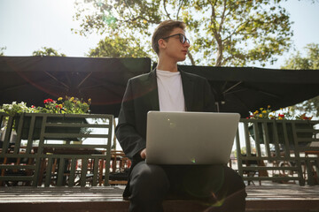 Successful confident mature business leader or manager, in formal suit, uses laptop, communicates via video conference, greetings colleagues during online meeting, waves his hand, smiles friendly