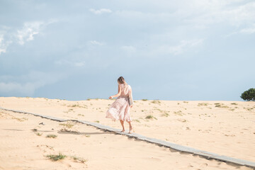 Lovely view of caucasian blond woman in long dress walking in desert with white sand on sunny day during summer vacation. Sand dunes.