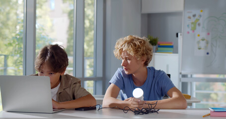 Teen schoolboys sitting at desk working on scientific project with laptop and sun battery in class