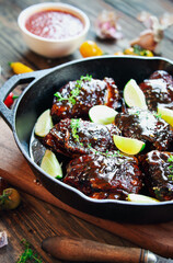 Spicy chili chicken thighs in a cast iron pan over a wooden cutting board with fresh ingredients. Selective focus on chicken in front of pan with blurred foreground and background.