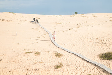 Picturesque view of beautiful blond woman in long casual dress walking in desert with white sand on sunny day during summer vacation. Sand dunes.