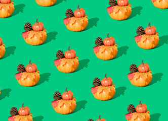 Creative autumn pattern made of pumpkins, pine cones and leaves on green background. Minimal seasonal concept. Halloween or Thanksgiving composition.