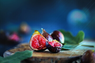 Whole and sliced fresh figs over a rustic cutting board background with leaves. Extreme selective...