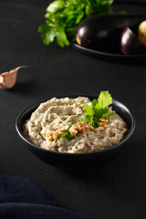 Baba ganoush from baked eggplant with parsley, garlic and olive oil on black table. Close up. Homemade Mediterranean Baba Ganoush. Vertical format.