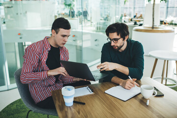 Focused colleagues working on laptop in modern workspace