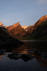 Fototapeta na wymiar Epic sunrise by an alpine lake in Switzerland called Seealpsee. The sun shines to the peak of the mountain on the other side of the lake. This looks so wonderful.