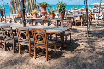 Celebration venue with wooden long table, chair, light bulb hanging and plant decoration in retro style on the beach