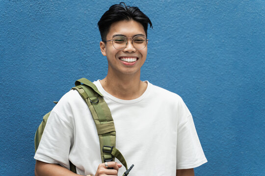 Portrait of Young Asian Philippines Teenager Student smiling over blue background - Smiling college guy with glasses