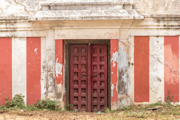 A vintage brown wooden door on the red striped walls of an ancient Hindu temple in a village in...