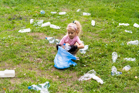 a little girl removes plastic garbage and puts it in a biodegradable garbage bag outdoors. The concept of ecology, waste processing and nature protection. Environmental protection