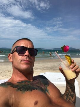 Man in dark sunglasses holding a drink on the beach