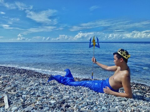 Man in king merman outfit lying on seashore