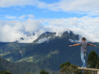 Man opening arms wide and standing on tree trunk while looking at mountain range in Ecuador