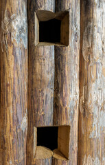 holes in a wooden wall made of logs old and weathered vertically