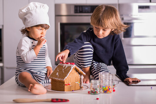 Two siblings sitting in kitchen making gingerbread house