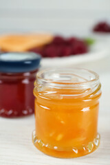 Open glass jar of sweet jam on white wooden table, closeup. Space for text