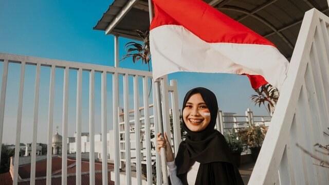 Woman in a hijab sitting on staircase holding Indonesian flag