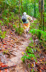 Tourist in rain poncho and helmet walks in jungle Thailand.