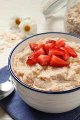 Tasty oatmeal porridge with strawberries served on table, closeup