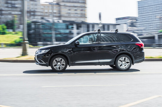 Black car Mitsubishi Outlander ES fast drive on asphalt road, side view.