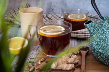 Healthy tea poured into transparent cup. Teapot, lemon, ginger, cardamom, heather bunch and glass...