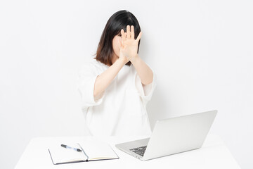 ノートパソコンを使いながら顔を隠す若い女性