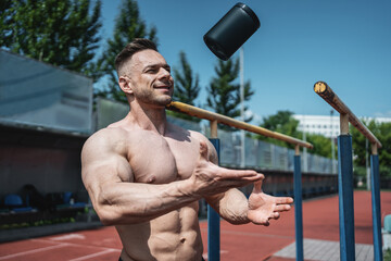 muscular athlete man throw up black container with protein whey powder outdoor
