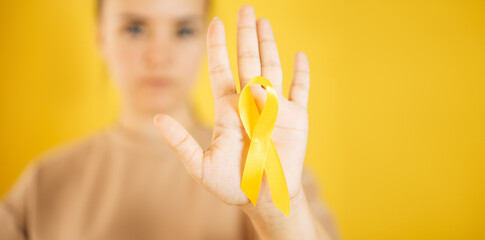 a woman holding a yellow gold ribbon in her hand on a yellow background, Bone cancer, awareness of childhood cancer, yellow September, the concept of World Suicide Prevention Day