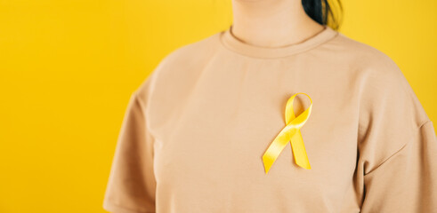 a woman holding a yellow gold ribbon in her hand on a yellow background, Bone cancer, awareness of childhood cancer, yellow September, the concept of World Suicide Prevention Day