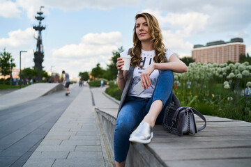 Fototapeta na wymiar Casual dressed female in casual clothes holding disposable caffeine beverage and modern smartphone device, thoughtful blogger with mobile phone spending coffee time in city thinking about tourism