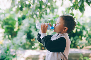 A little boy drinks water outdoors from a blue bottle