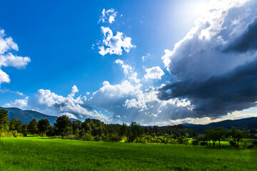 Obraz premium Green meadow in a day with white and gray clouds and sun rays.
