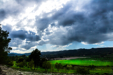 Obraz premium Green meadow in a day with white and gray clouds and sun rays.