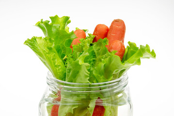 Lettuce leaves and carrots in a glass transparent bottle on a light background