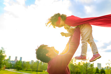 happy african american little fearless girl flying outdoor on father's hands in summer park