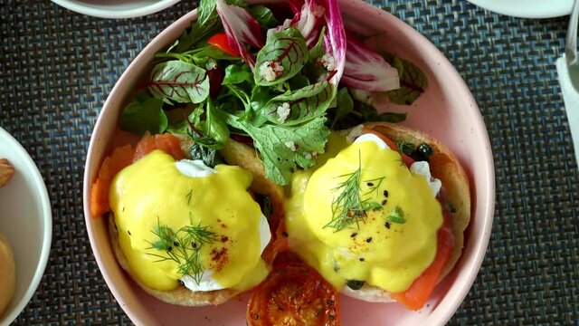 Top View of Fresh Poached Eggs with Salmon on Baked Bread with Grilled Vegetable and Green Salad. Close-up of Healthy Tasty Breakfast in Hotel. Benedict Eggs with Muffin and Tomato in Trendy Plate. 4k