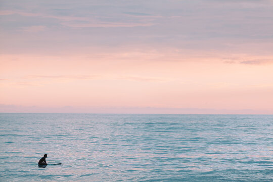 Lone surfer at sunset in the calm ocean.