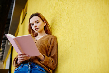 Serious woman reading diary near yellow wall