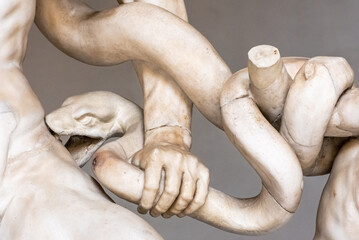 Close-up on marble statue of snake biting a man´s thigh - obrazy, fototapety, plakaty