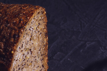 Slice of rustic natural yeast-free bread with flax, poppy seeds, sesame seeds, millet, pumpkin and sunflower seeds, on a black background, hard light, photo in a low key.