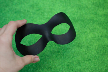 Black carnival mask in a woman's hand on a light green background