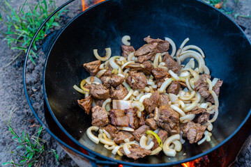 Process of cooking of delicious pilaf - fried meat with onion in a cauldron outdoor