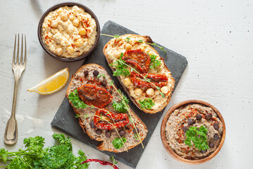 Hummus and black chickpea hummus on black bread with sun-dried tomatoes. In a plate hummus and black chickpea hummus