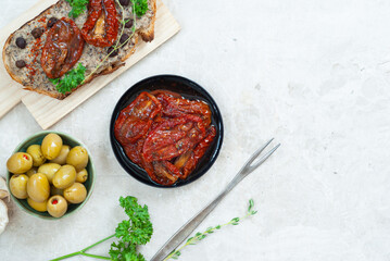 Sun dried tomato with a slice of bread with hummus and a plate of olives