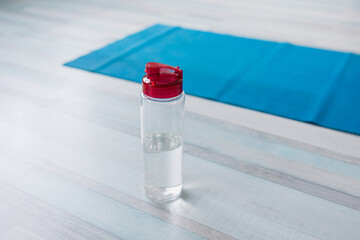blue yoga mat and sports bottle stands on the floor, yoga preparation or training, sports at home during self-isolation and pandemic, training programs with a personal trainer online, taking care of