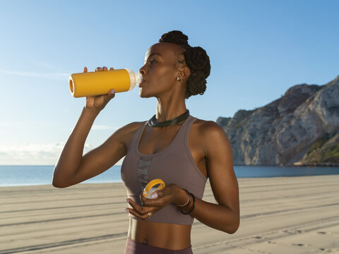 Black jogger drinking water on beach