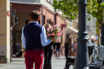 An elegantly dressed man, carrying a bouquet of flowers, follows the blurry silhouette of the departing woman
